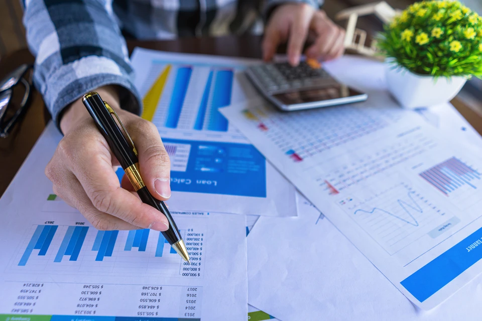 Personne en chemise travaillant sur documents financiers avec graphiques et tableaux de données