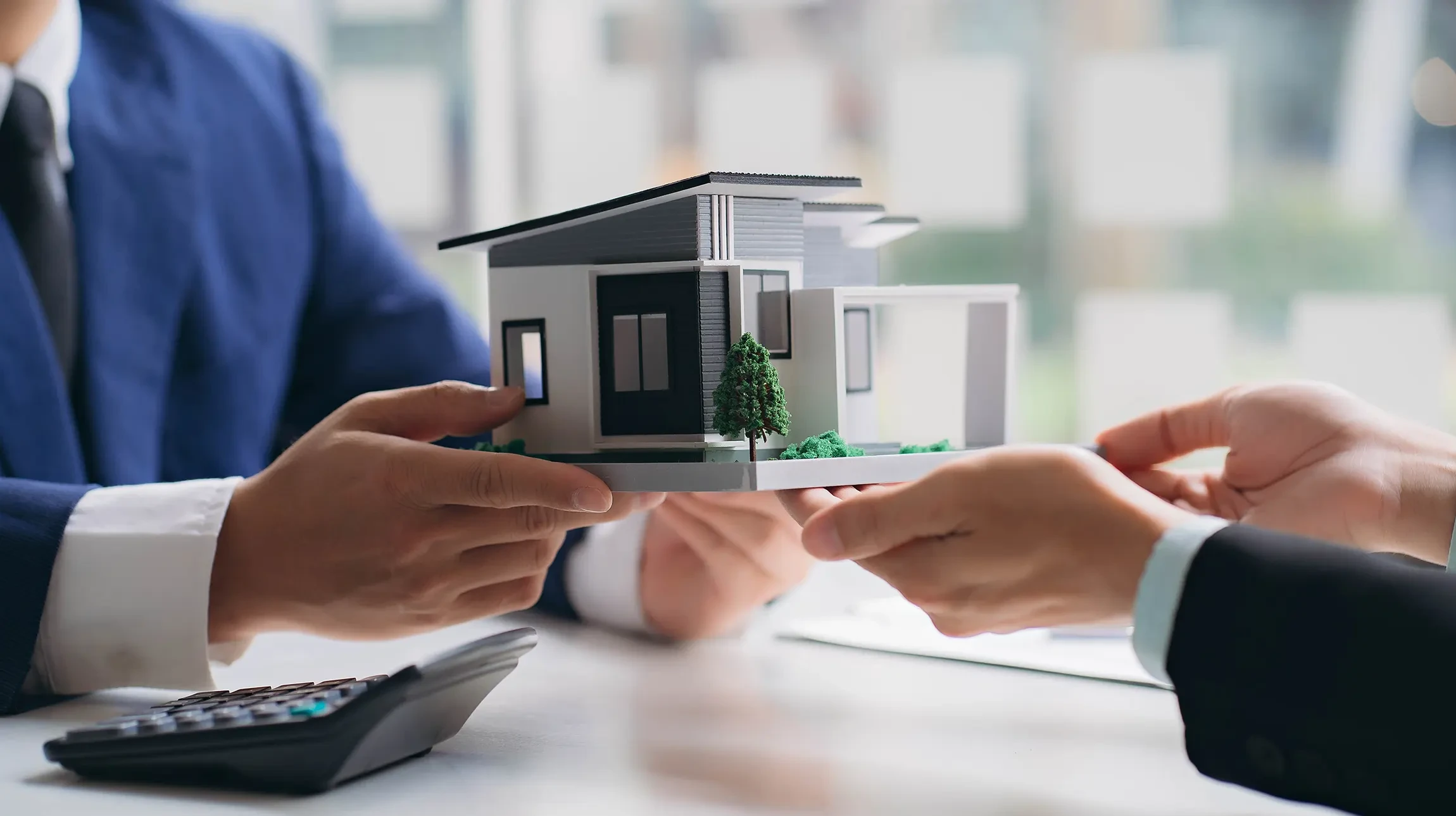 Un homme et une femme allongés face à face de chaque côté d'une maquette de maison en carton, symbolisant la séparation ou le partage immobilier